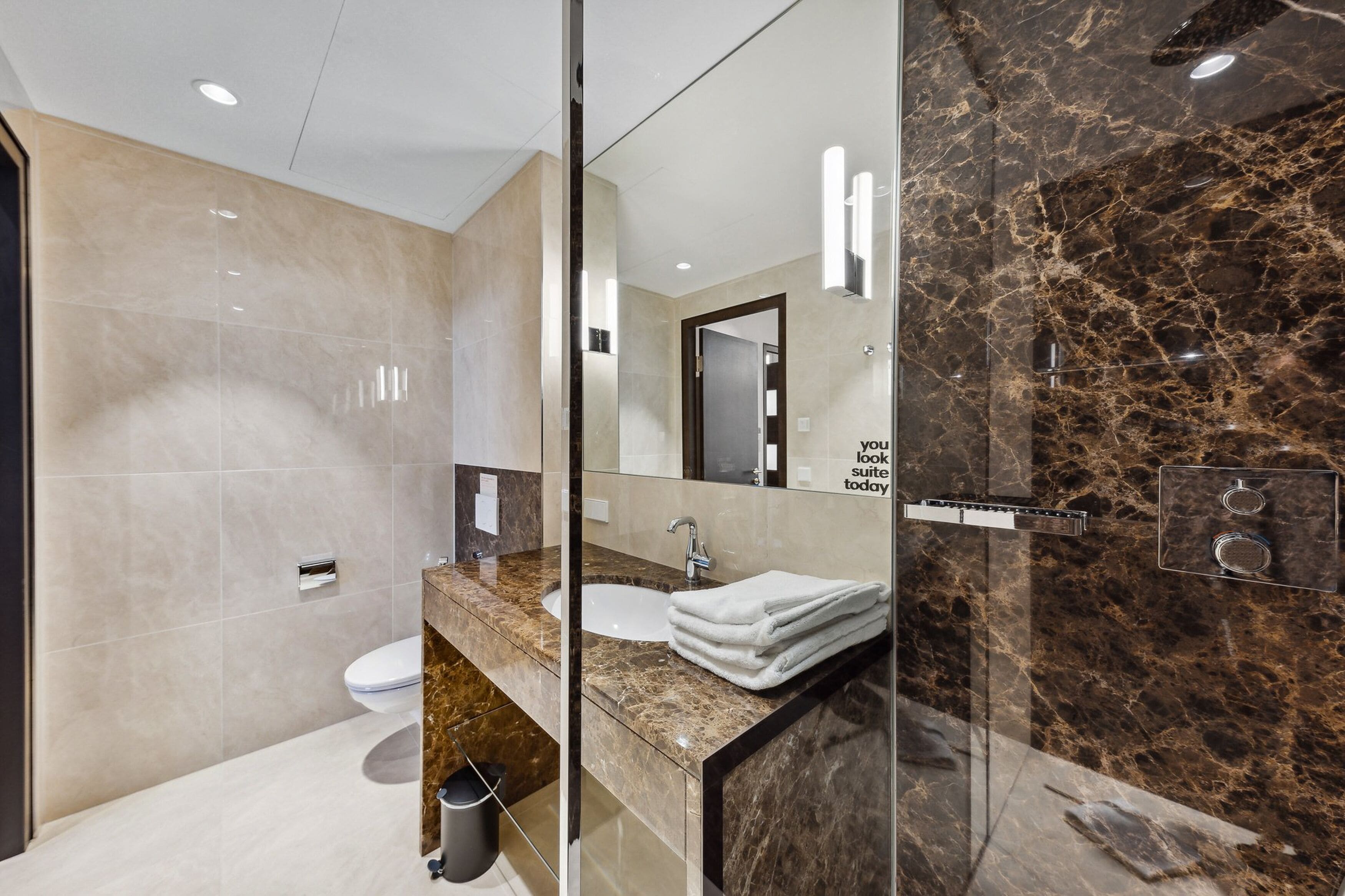 A modern bathroom with a marble sink, a glass shower enclosure, and a large mirror.