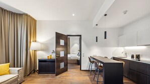 A modern hotel room with a sofa, a desk, a kitchenette, and a bathroom visible through an open door. - Limehome Vienna Roßauer Lände (Vienna)