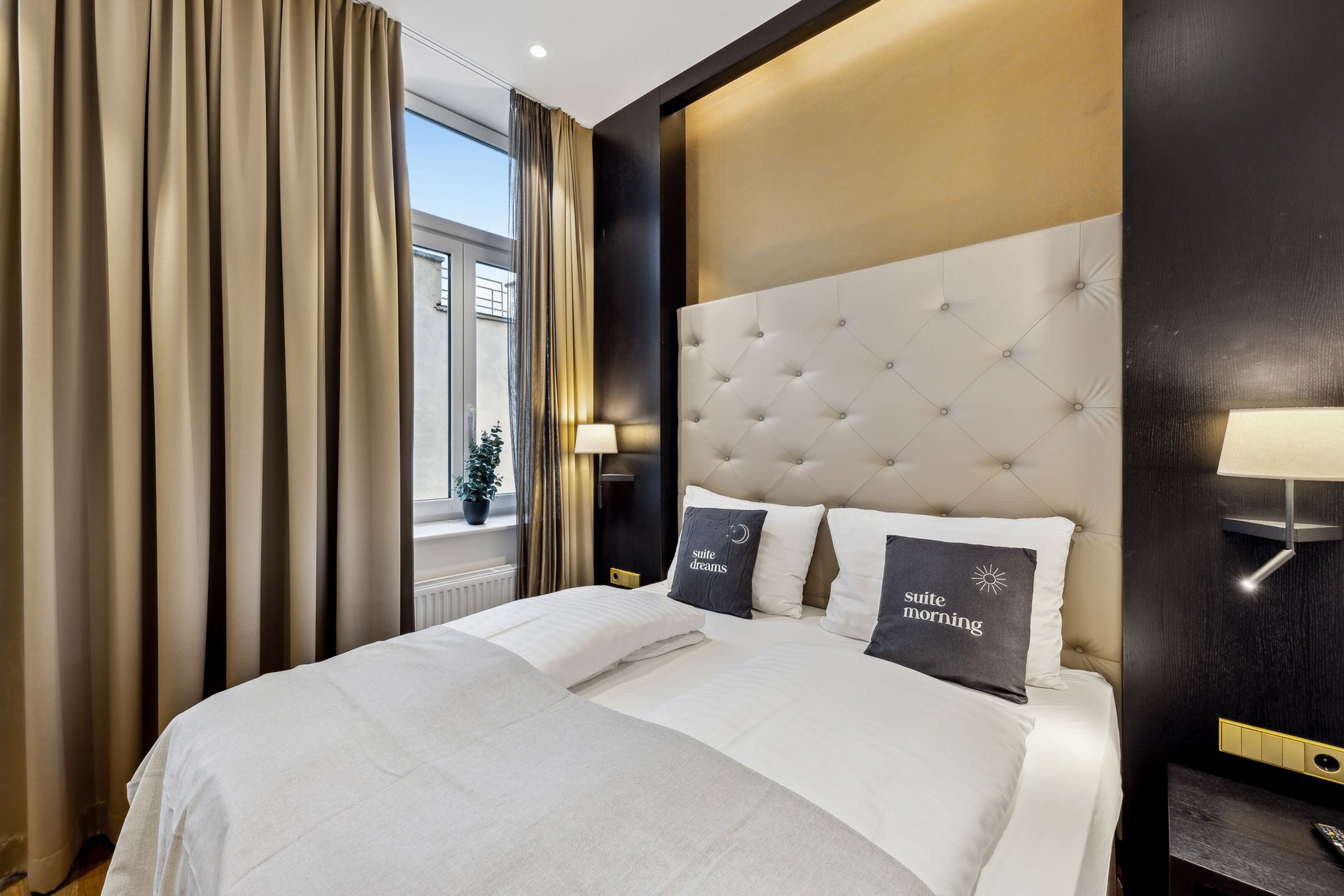 Una habitación de hotel con una cama grande, un cabecero tapizado y dos lámparas de noche.