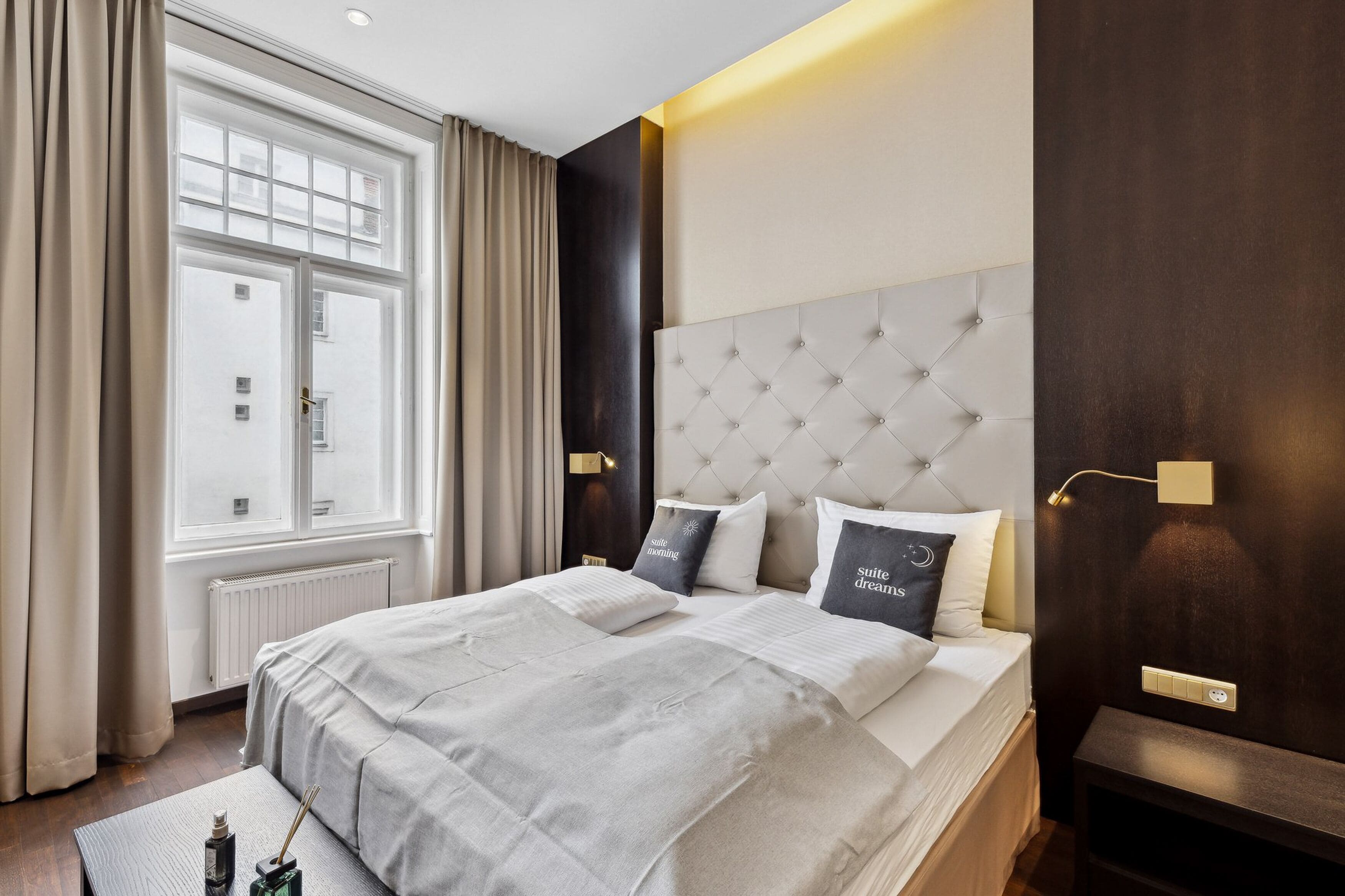 Een moderne hotelkamer met een groot bed, een raam met gordijnen, een donker houten hoofdeinde en een nachtkastje.