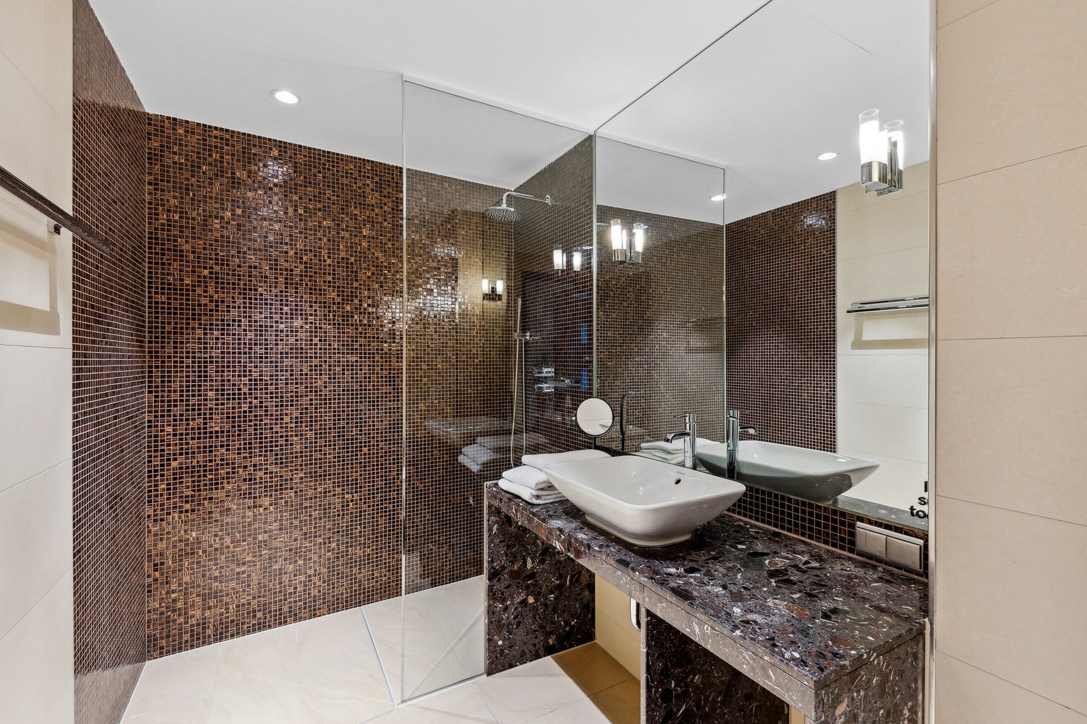 A modern bathroom with a large mirror, two sinks, and a shower area.