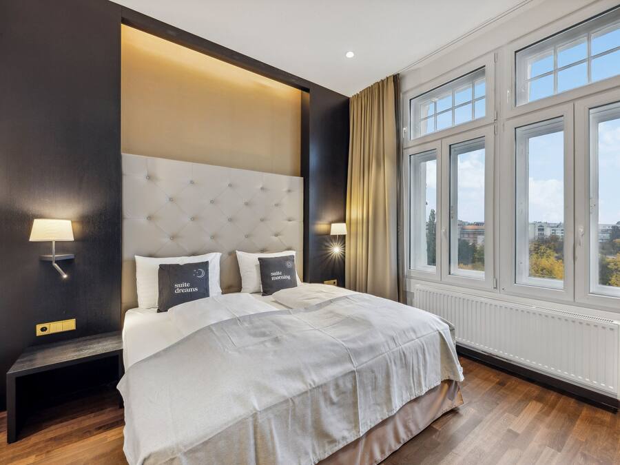 Habitación de hotel con una cama grande, dos lámparas de noche, una ventana con cortinas y vistas a la ciudad.