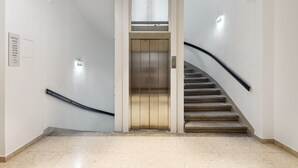 A modern elevator with a metallic finish, a staircase with a black handrail, and a tiled floor. - Limehome Vienna Roßauer Lände (Vienna)