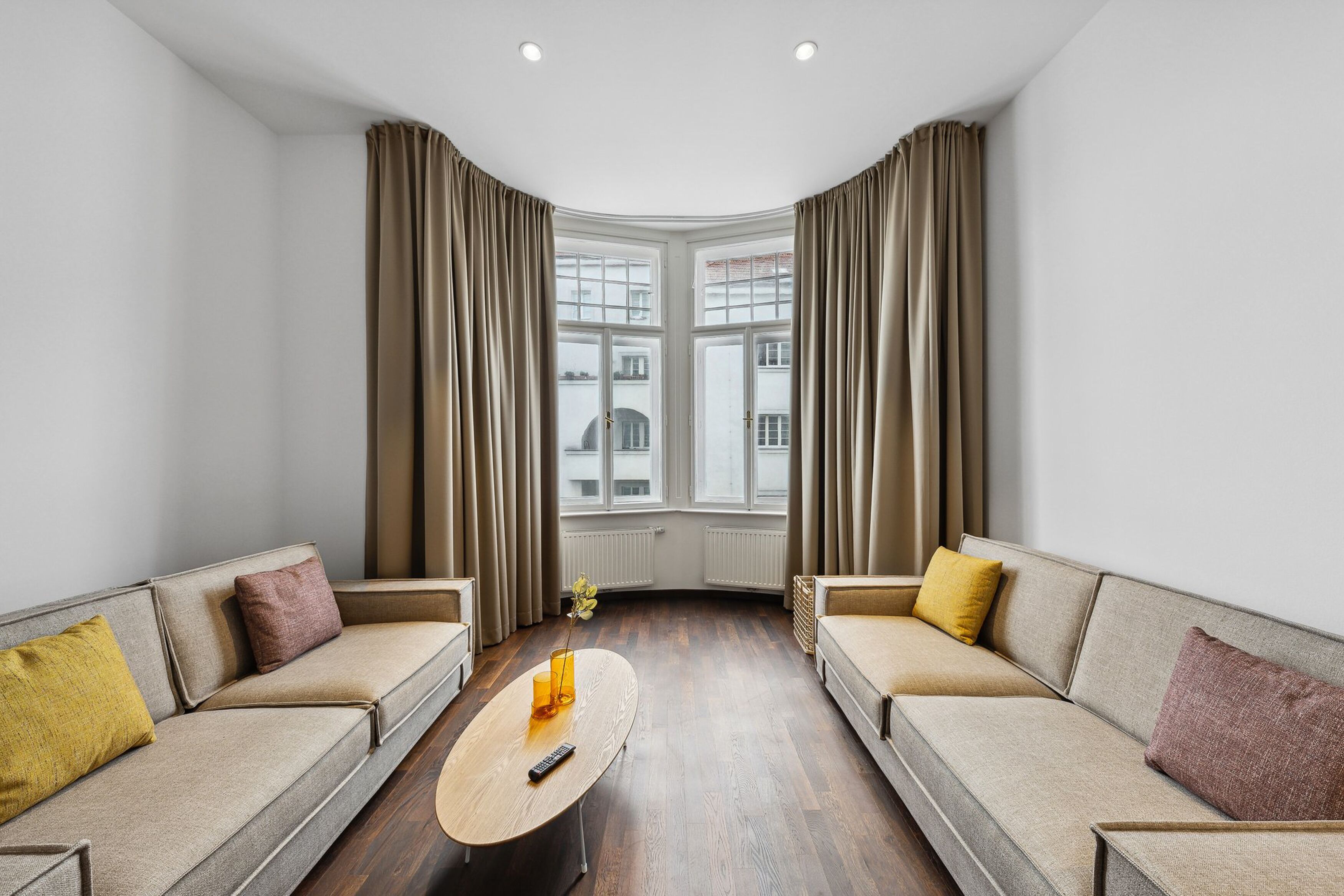 A modern living room with two sofas, a coffee table, and a view of buildings through large windows.