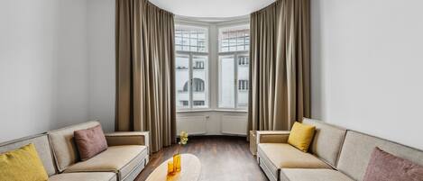 A modern living room with two sofas, a coffee table, and a view of buildings through large windows.