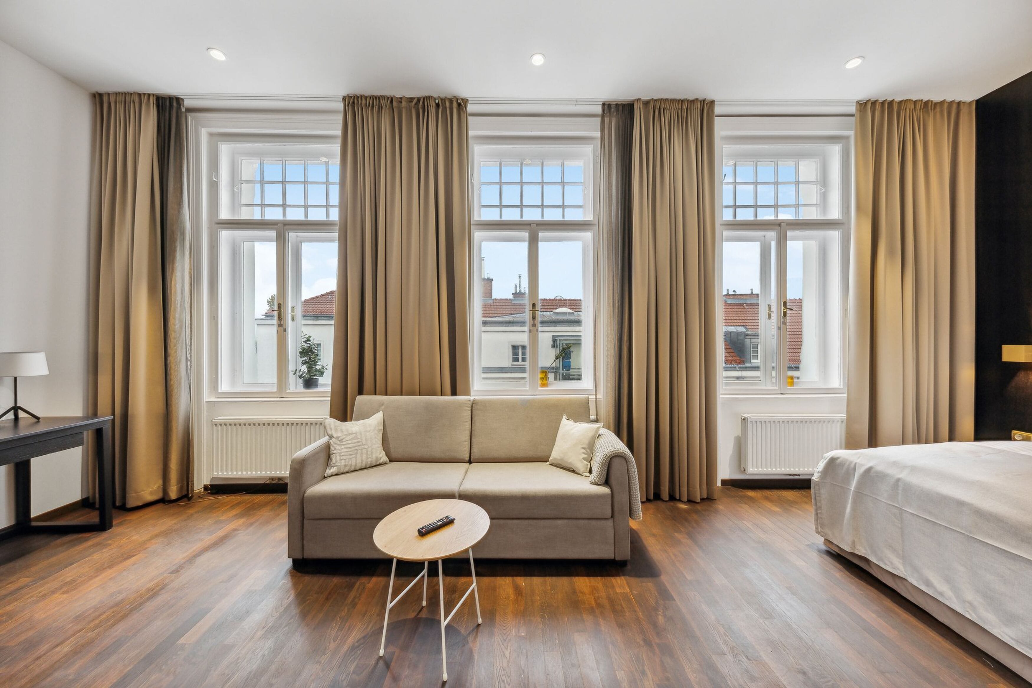 Een moderne hotelkamer met een beige bank, een klein rond tafeltje en een bed.