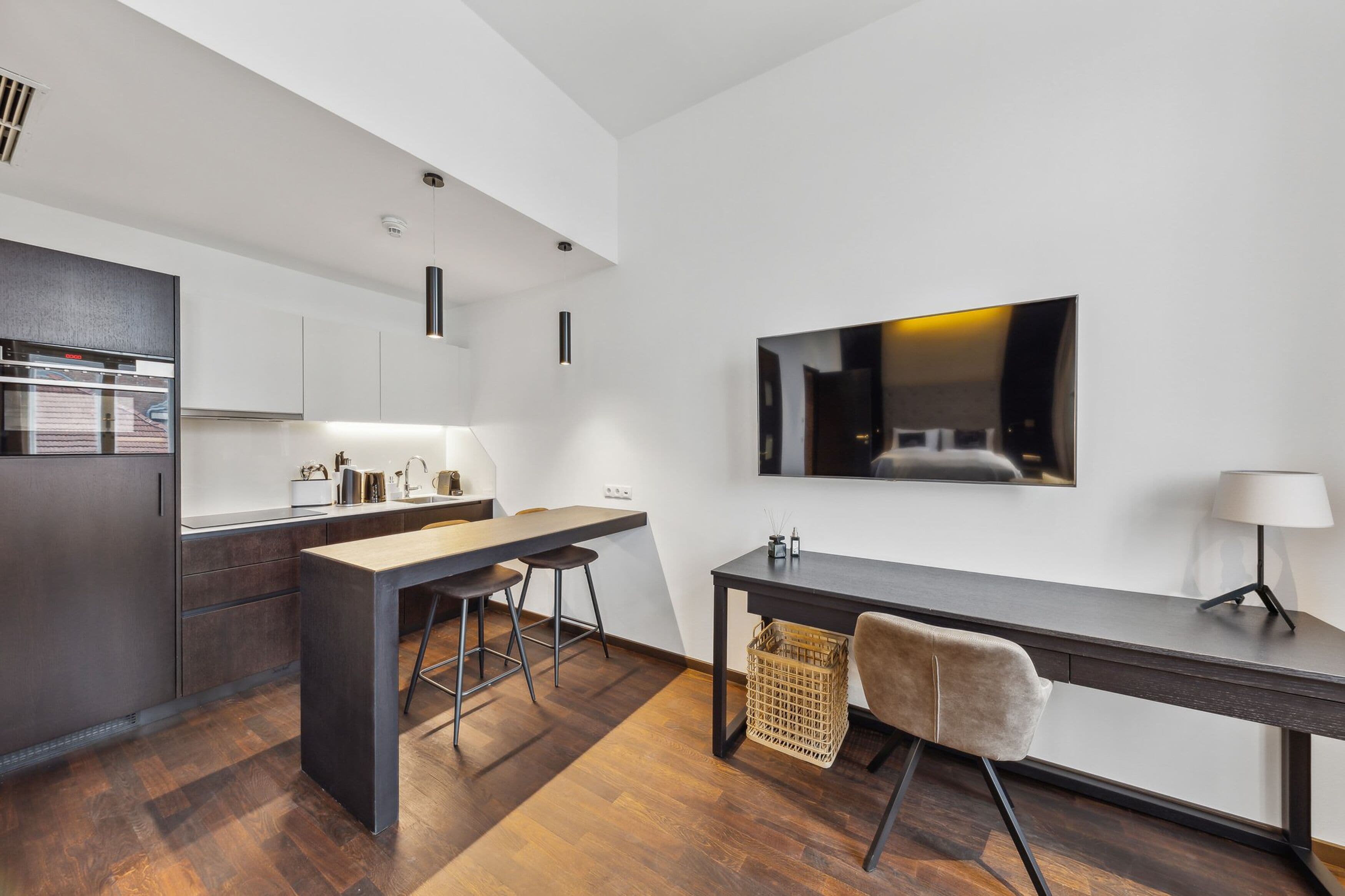 A modern kitchen with a central island, bar stools, a dining table, and a large flat-screen TV mounted on the wall.