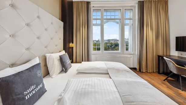 A hotel room with a large bed, a desk, and a view of the city. - Limehome Vienna Roßauer Lände (Vienna)