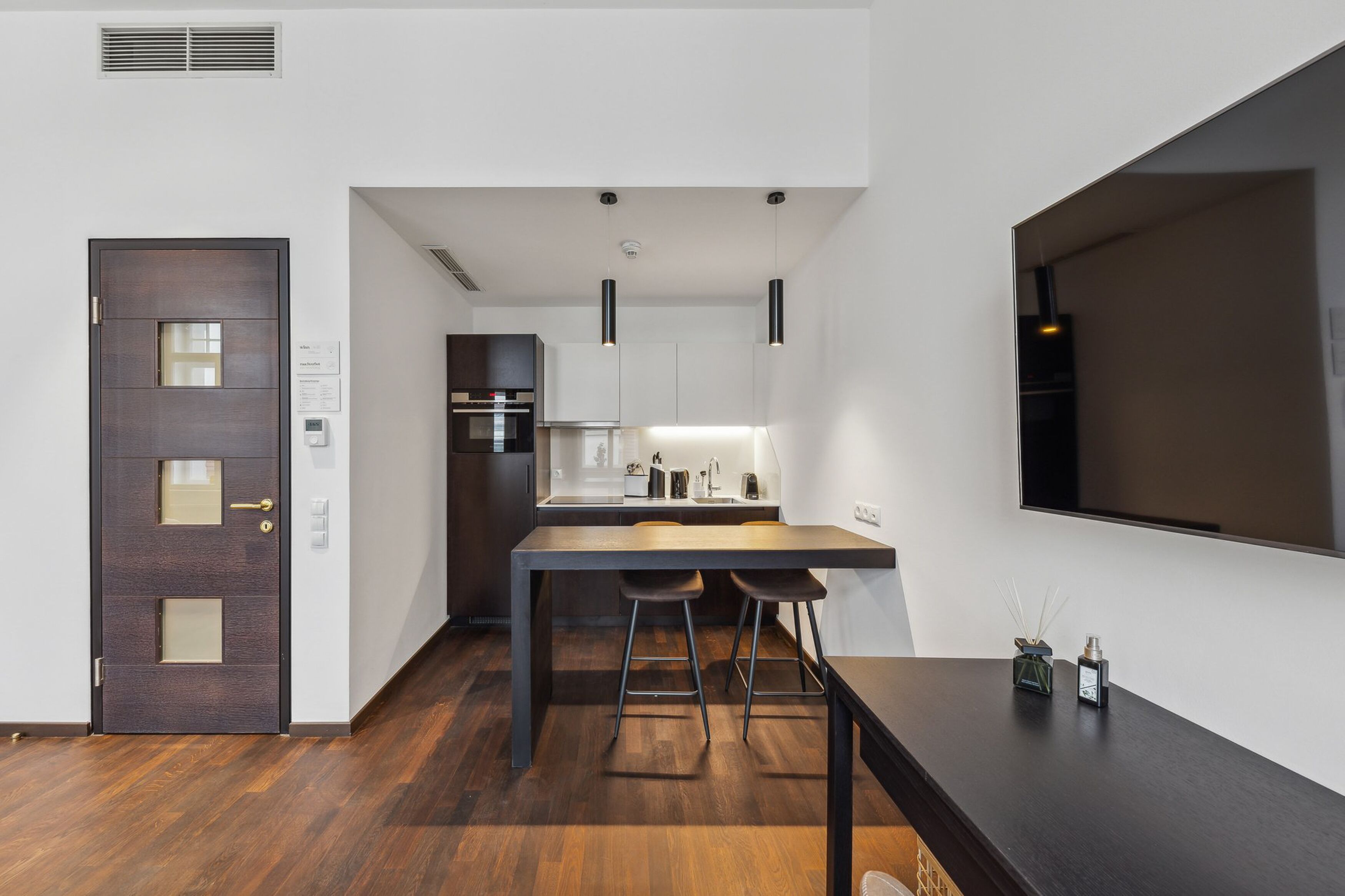 A modern kitchen with a dark wooden table, two bar stools, and pendant lighting.