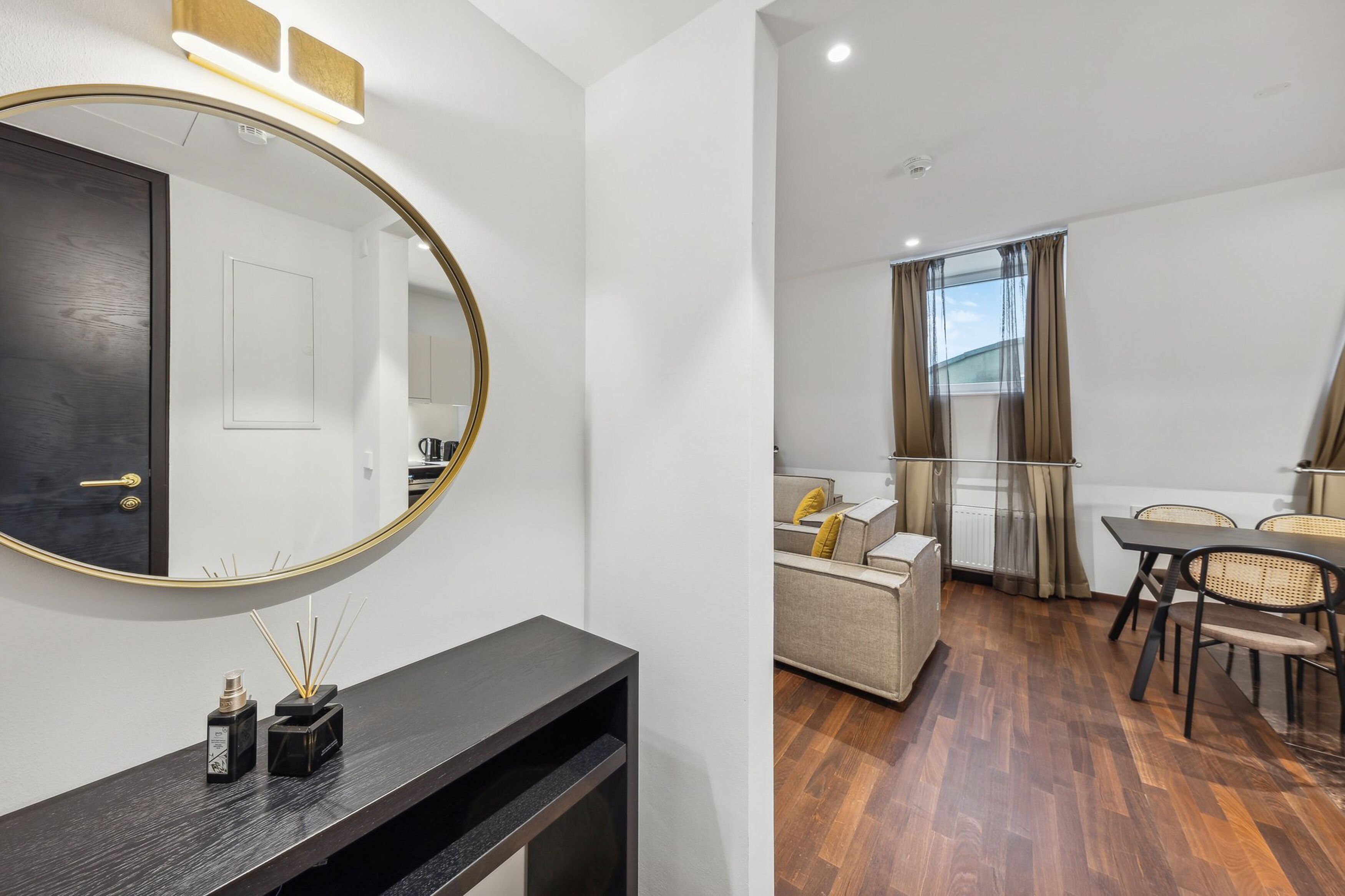 A modern living room with a sofa, a dining table with chairs, a large mirror, and a dark console table.