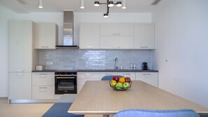 A modern kitchen with white cabinets, a wooden table, and a fruit bowl. - Villa Blauw with Infinity Pool  (LEFKADA)