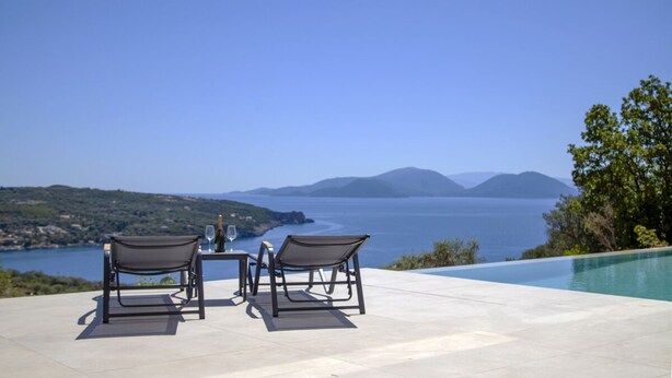 A terrace with two chairs and a table, overlooking a body of water and distant mountains. - Villa Blauw with Infinity Pool  (LEFKADA)