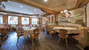 A restaurant with wooden furniture, large windows, and a mural on the wall. - Hotel Forellenhof (Saalbach-Hinterglemm)
