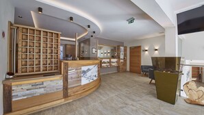 A modern hotel lobby with a wooden reception desk, a large mirror, and a fireplace. - Hotel Forellenhof (Saalbach-Hinterglemm)