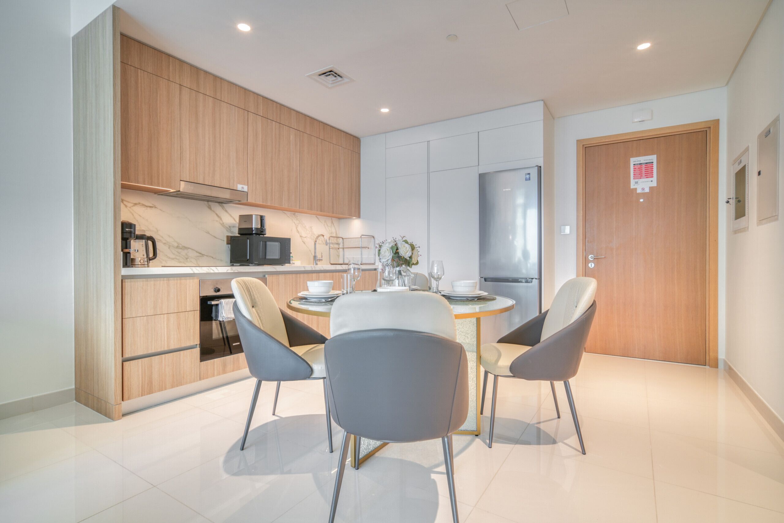 Een moderne keuken met houten kastjes, een roestvrijstalen koelkast, en een eethoek met een ronde tafel en vier stoelen.