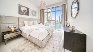 A modern hotel bedroom with a large bed, a nightstand, a dresser, and a city view through the window.