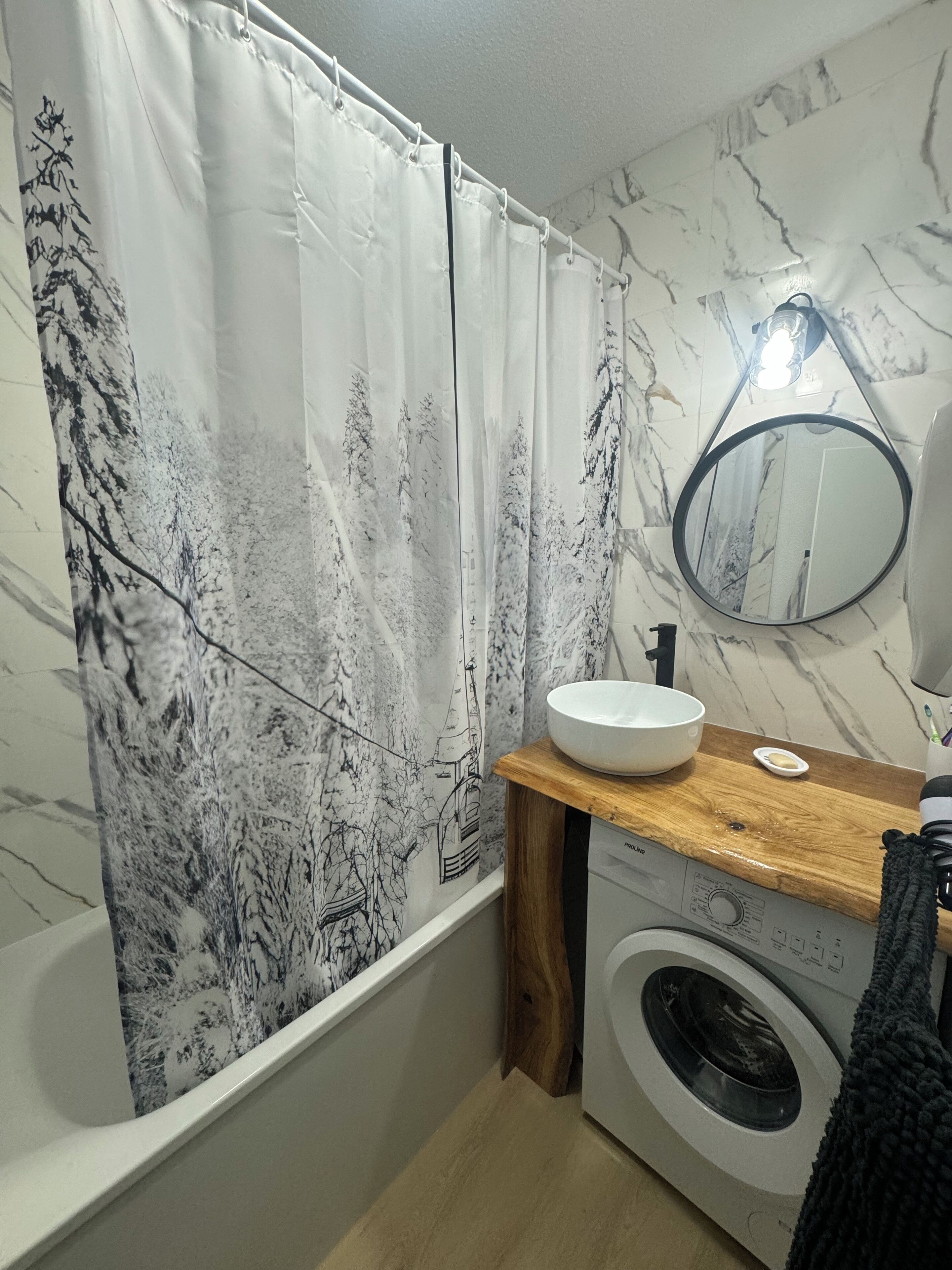 A bathroom with a washing machine, a sink, a mirror, and a shower curtain with a tree design.