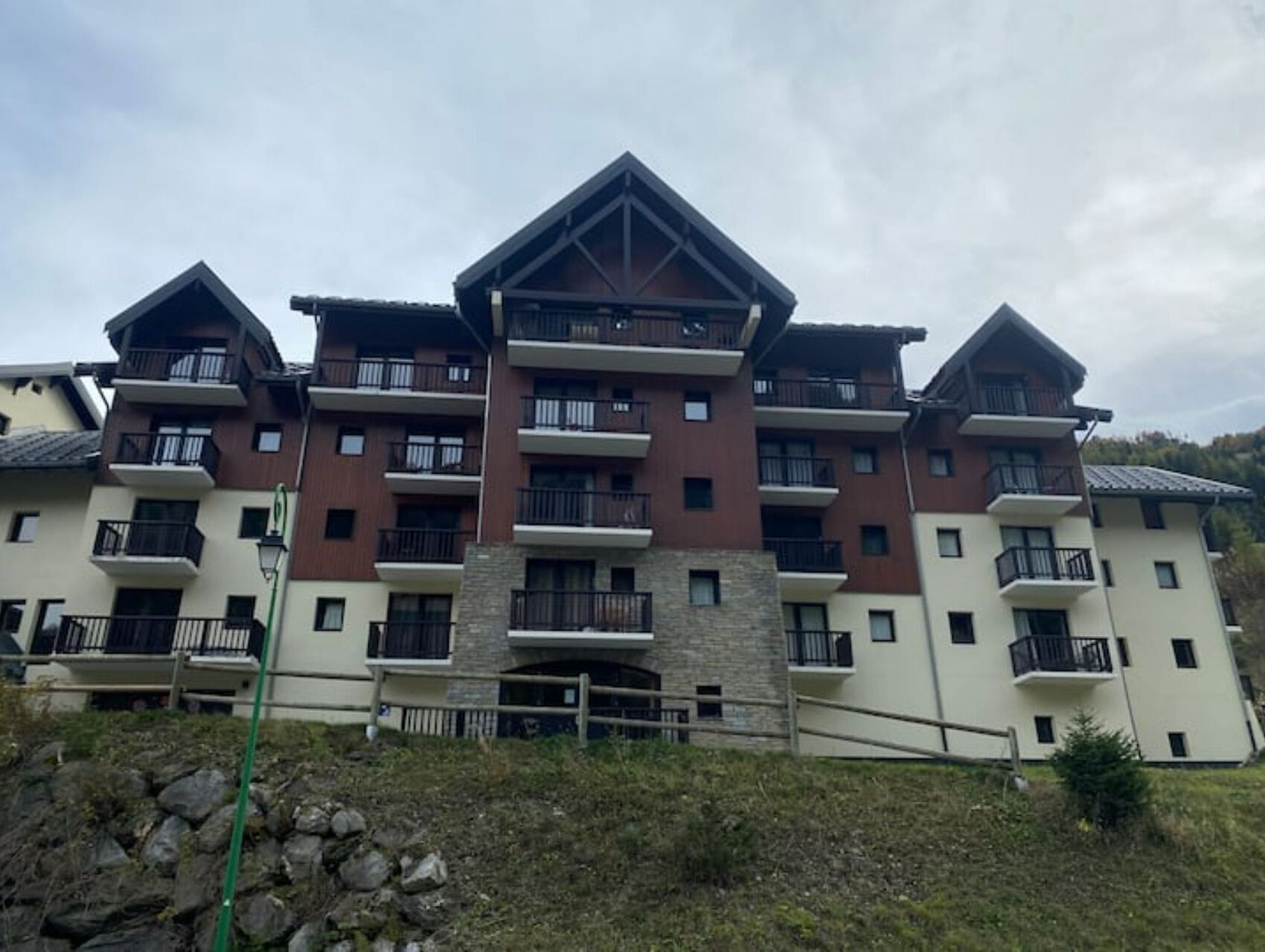 A multi-story hotel with balconies, a stone facade, and a mountainous backdrop.