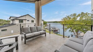 Ein geräumiger Balkon mit einer grauen Couch und einem Tisch, mit Blick auf einen See und ein Gebäude.