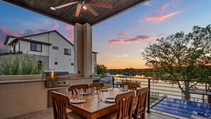 Eine Terrasse im Freien mit Esstisch für vier Personen, Grill und Blick auf einen See bei Sonnenuntergang.