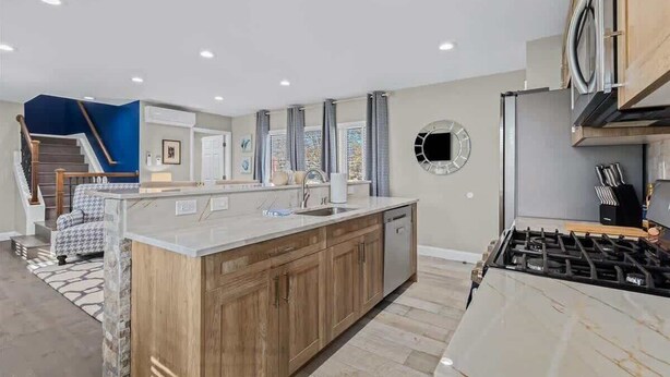 A modern kitchen with a central island, stainless steel appliances, and a view of a staircase leading to a living area. - Exquisite Apt near Beaumont (Royal Oak)