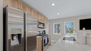 A modern kitchen with stainless steel appliances, wooden cabinets, and a marble countertop. - Exquisite Apt near Beaumont (Royal Oak)