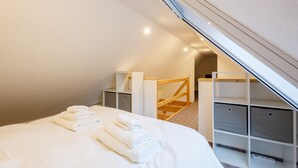 A bedroom with a bed, neatly folded towels, a wooden staircase, and built-in storage units. - Exklusives Tiny House in Elbnähe (Buxtehude)