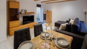 A modern living room with a wooden TV stand, a sofa, and a dining table set for four. - Exklusives Tiny House in Elbnähe (Buxtehude)