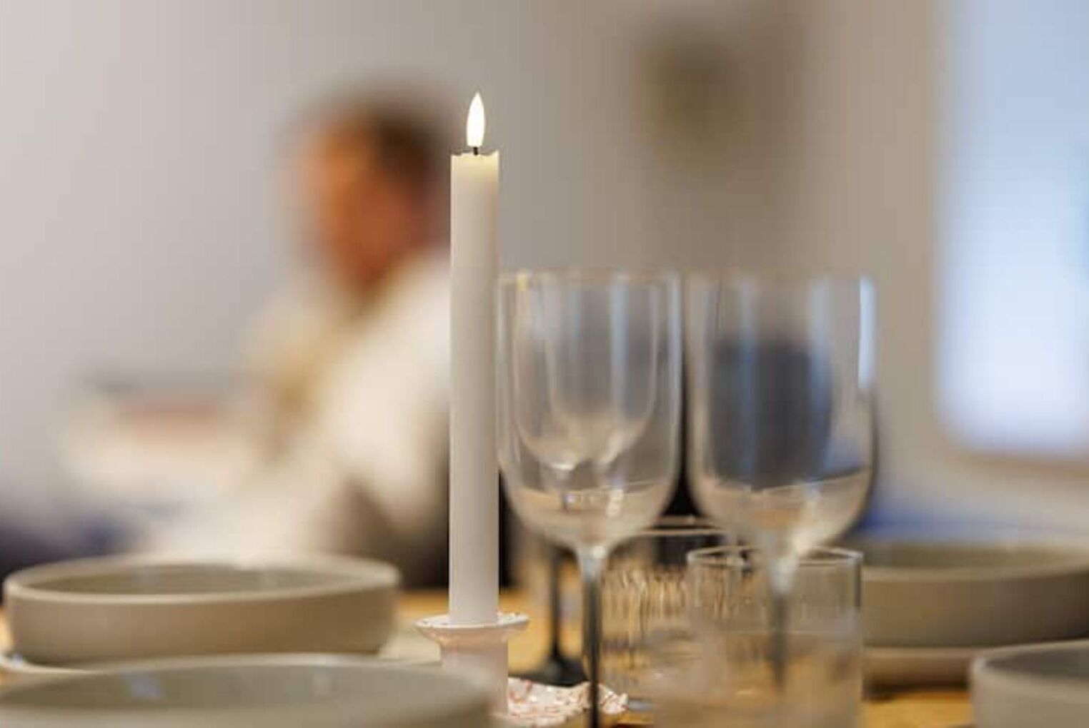 Una vela sobre una mesa con vasos y platos, que sugiere un ambiente para comer.