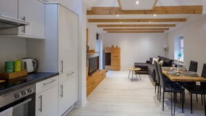 A modern kitchen with white cabinets, a stove, and a dining area with a table and chairs. - Exklusives Tiny House in Elbnähe (Buxtehude)