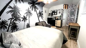 A bedroom with a bed, a desk, and a kitchenette.