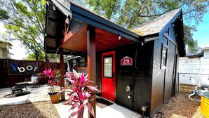 A small building with a red door, a sign reading "278 Tampa No Casa," and outdoor seating with chairs and tables.
