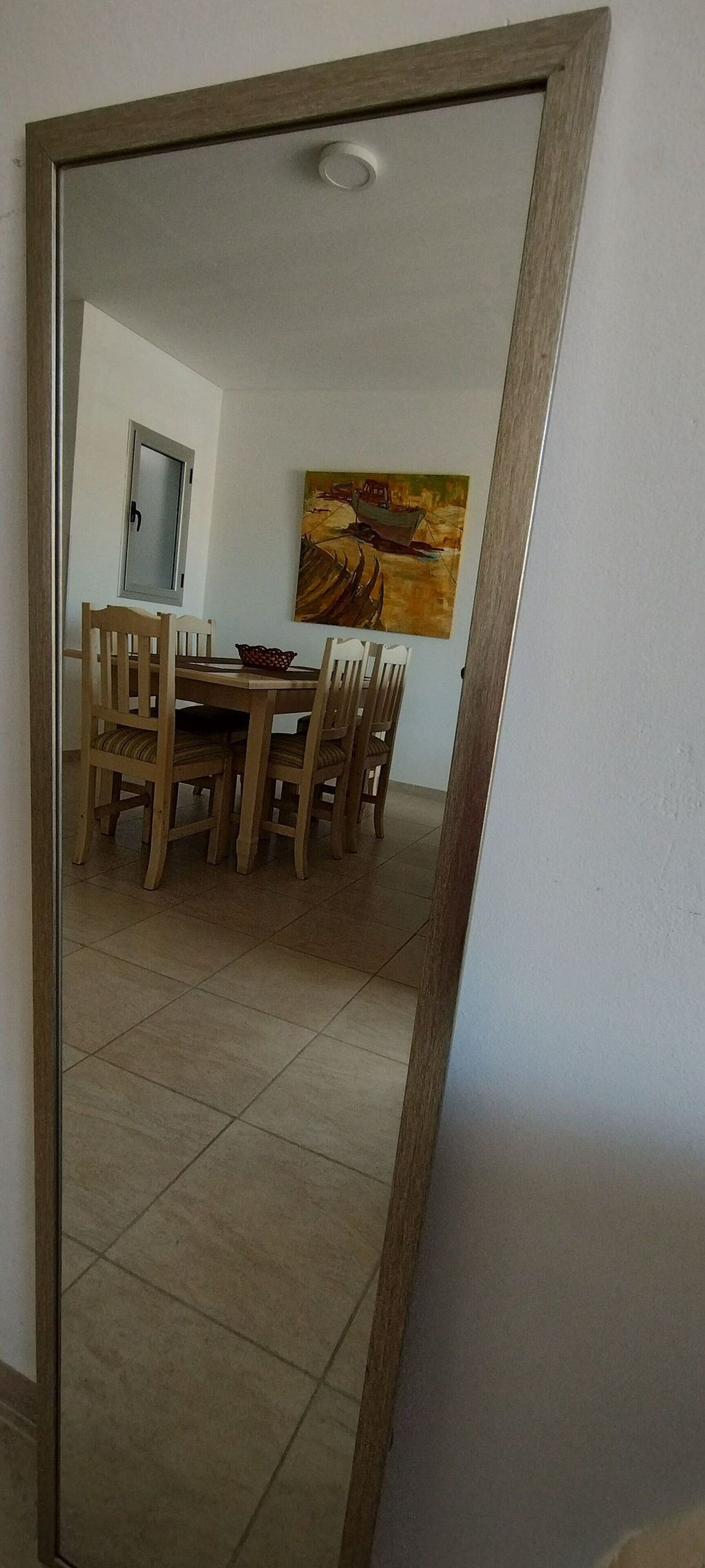 Una zona de menjador amb una taula i cadires de fusta, un quadre a la paret i una porta amb manilla.