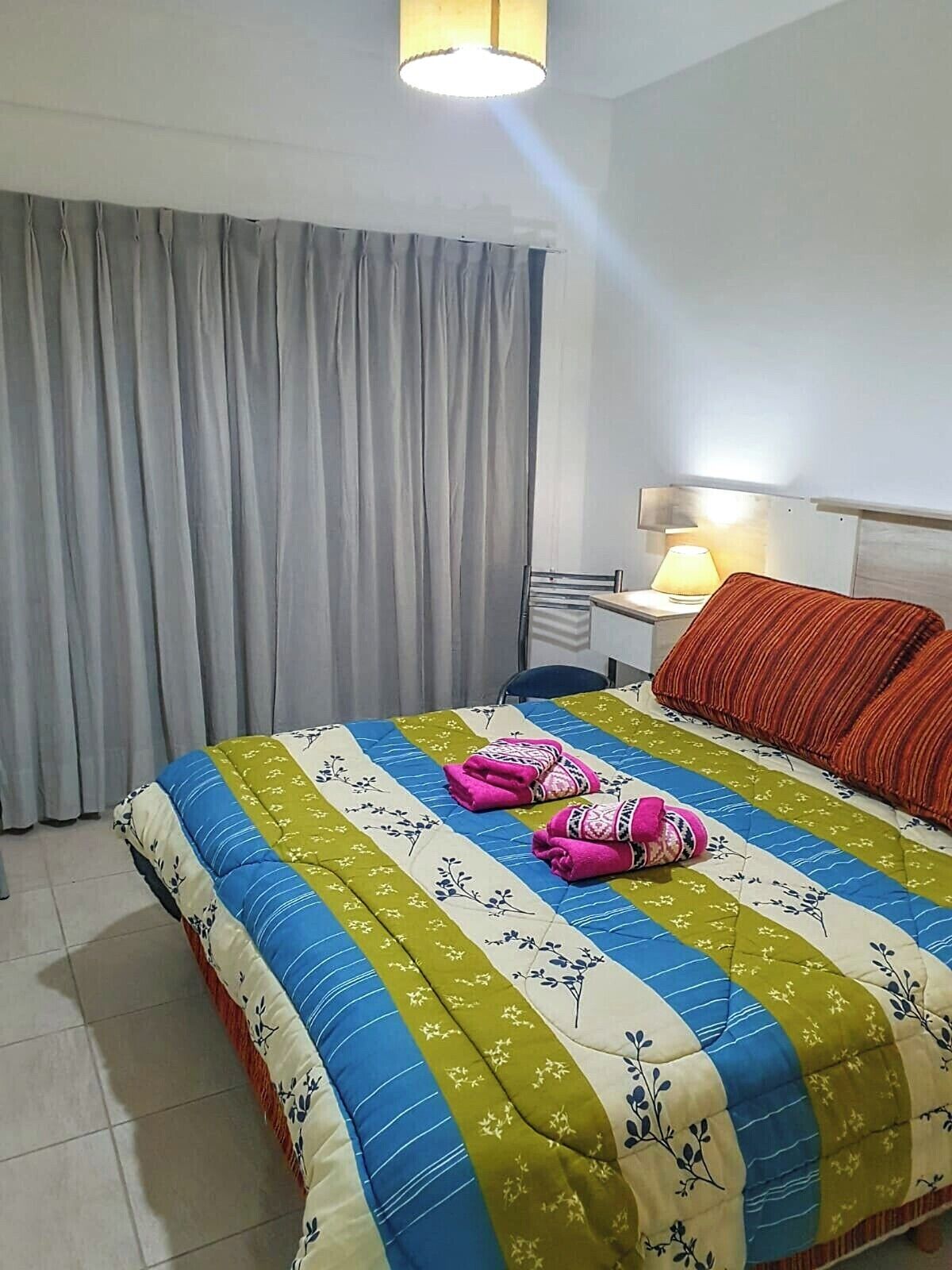 A hotel room with a bed, a nightstand, a lamp, and a window with curtains.