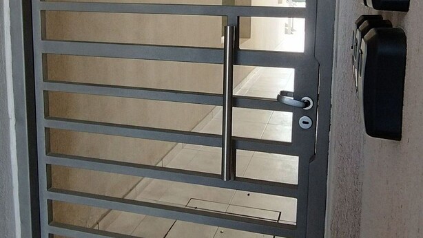 Une porte métallique avec des barreaux horizontaux, une poignée de porte et un trou de serrure.