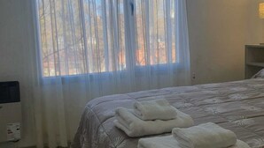 Une chambre à coucher avec un lit, une fenêtre ornée de rideaux légers et une table de chevet avec une lampe.