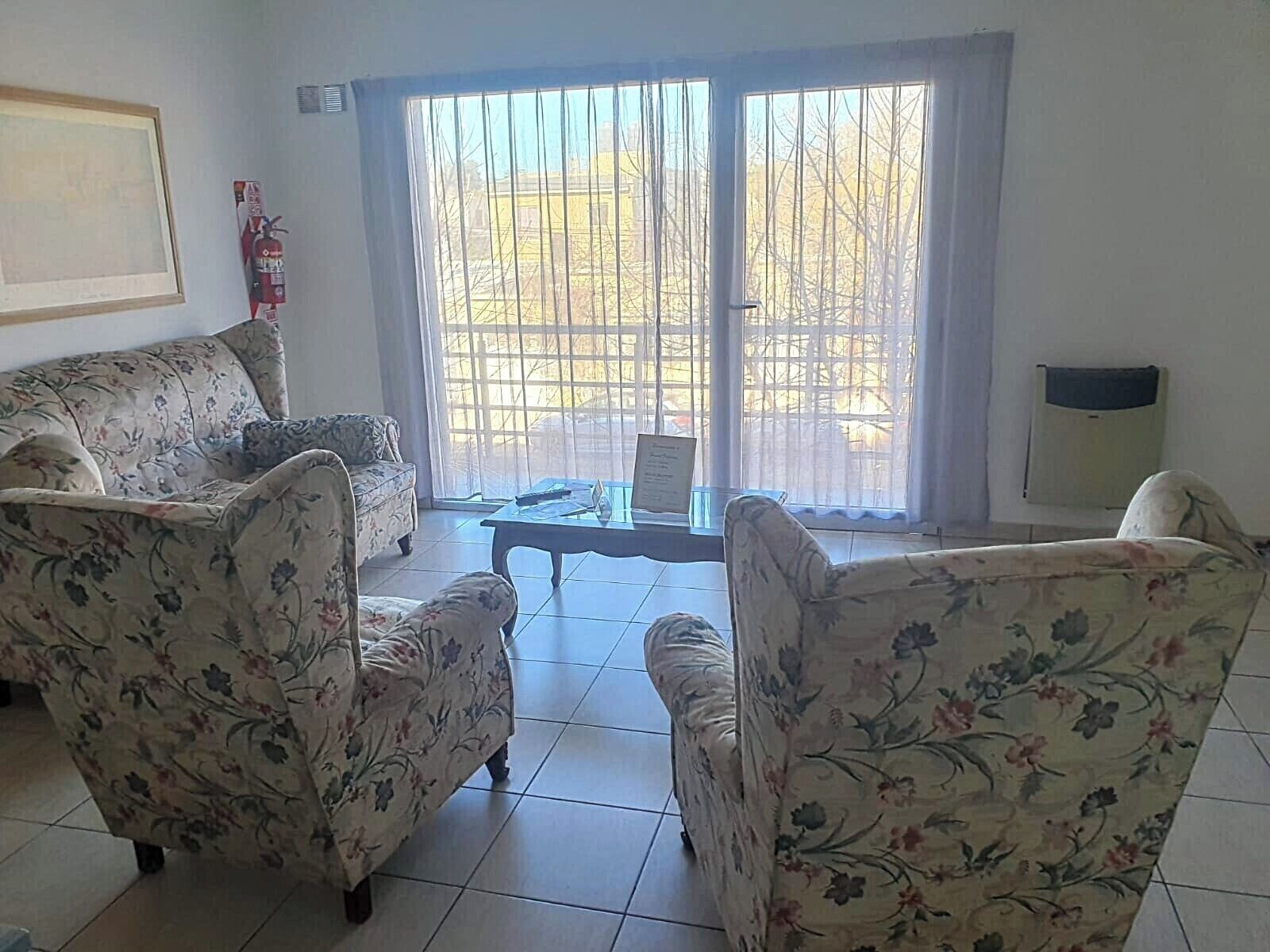 A living room with floral-patterned sofas, a glass coffee table, and a sliding glass door leading to an outdoor area.