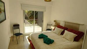 Une chambre à coucher comprenant un lit, une chaise, un bureau et une porte-fenêtre coulissante donnant sur un balcon.