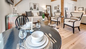 Ein Essbereich mit einem runden Tisch für vier Personen, einer Couch und zwei Sesseln in einem Loftsessel mit freiliegenden Holzbalken.