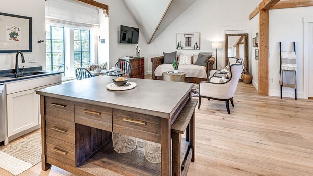 Ein geräumiges Loft mit Küche, Essbereich und Wohnbereich. Es bietet einen großen Holztisch, eine Küche mit Einbauofen und eine gemütliche Sitzecke mit Sofa und Sesseln.