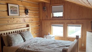 A wooden-paneled bedroom with a bed, a framed picture, and two windows.