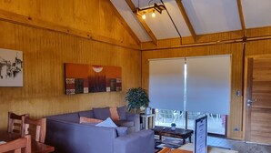 A cozy living room with a wooden ceiling, a sofa, a coffee table, and a large window. - Refugios de Montaña Reloncaví - RL1 (Pinto)