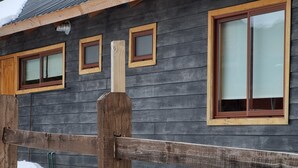 A wooden cabin with multiple windows, a wooden fence, and a snow-covered ground. - Refugios de Montaña Reloncaví - RL1 (Pinto)