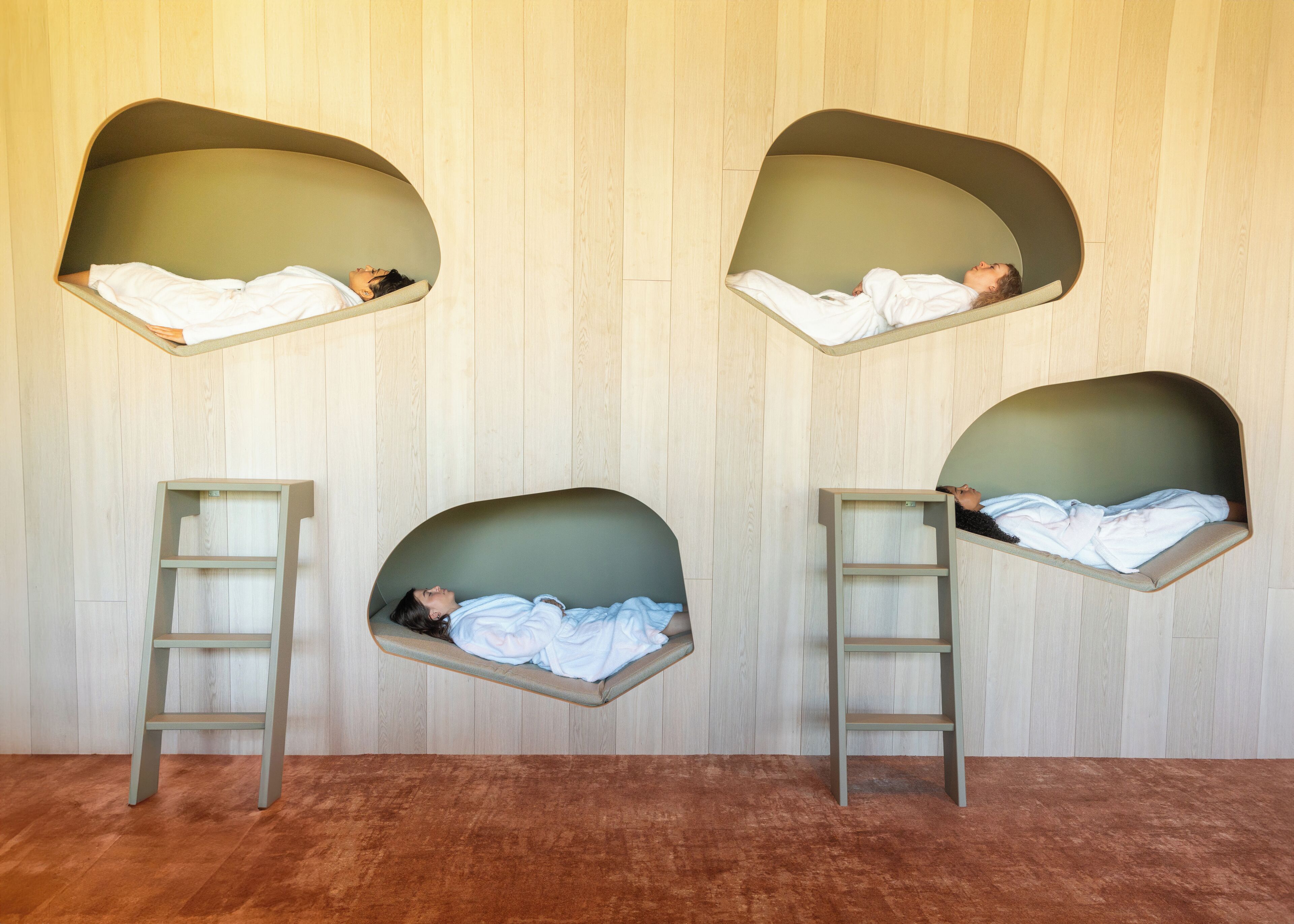 A room with four sleeping pods against a wooden wall, each with a ladder for access.