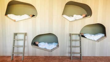 Una habitación con cuatro cápsulas para dormir adosadas a una pared de madera, cada una con una escalera para acceder.