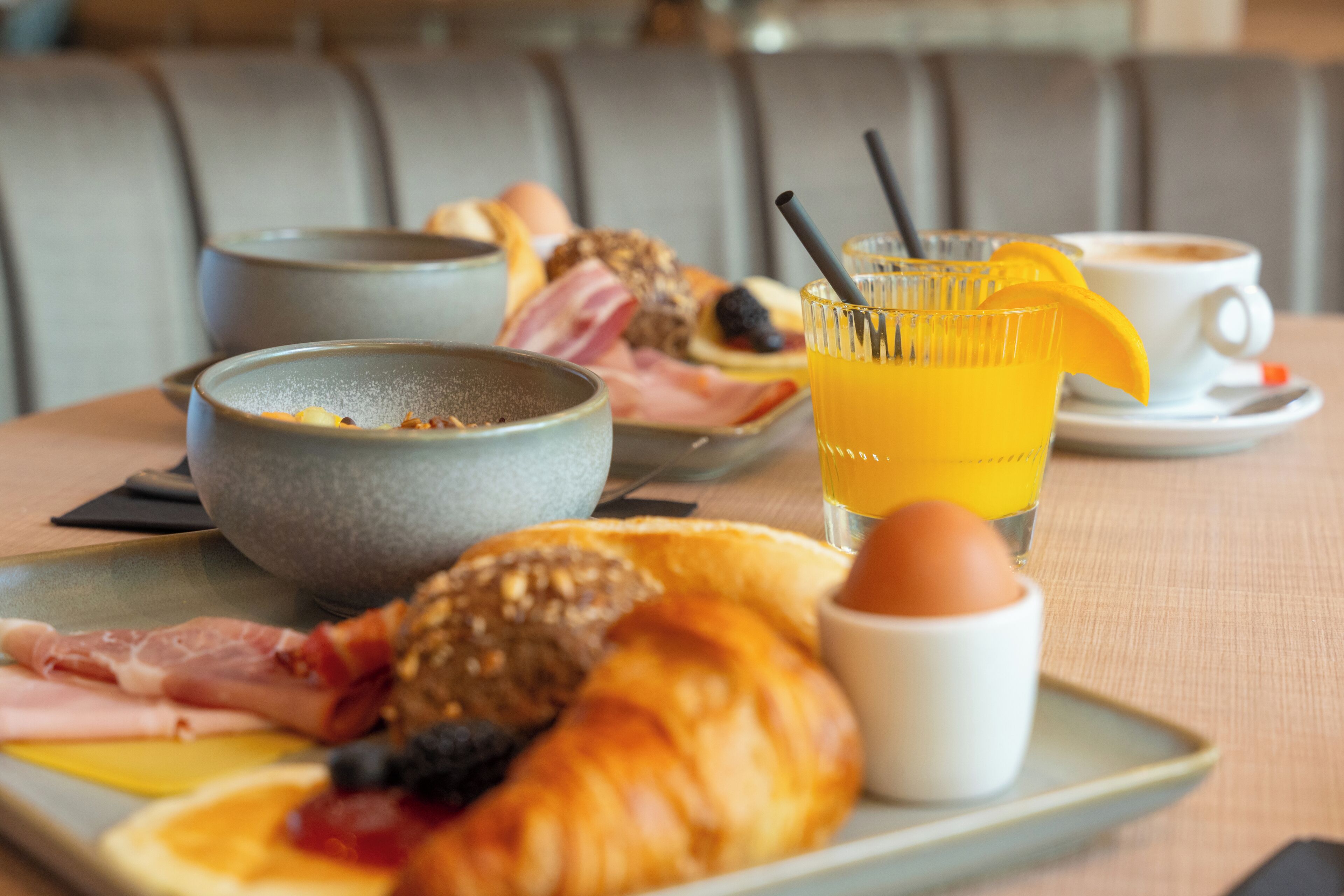 A breakfast tray with croissants, eggs, bacon, and a glass of orange juice on a table.
