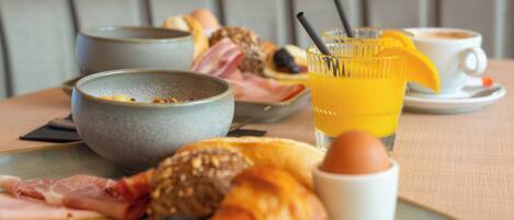 A breakfast tray with croissants, eggs, bacon, and a glass of orange juice on a table.