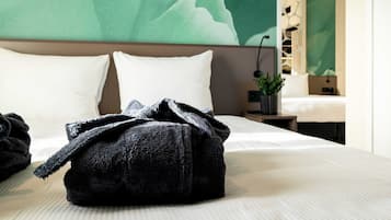 Uma cama bem arrumada com uma mala preta em cima, uma parede verde e uma pequena planta em uma mesa de cabeceira.