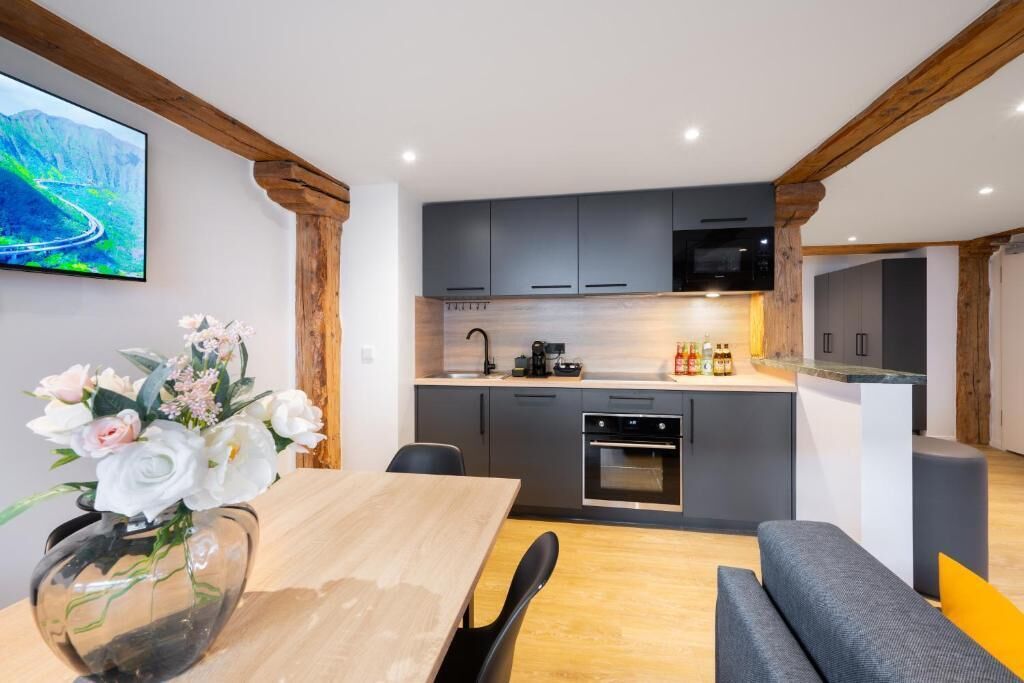 Une cuisine moderne avec des meubles gris, une table à manger en bois et un téléviseur fixé au mur.