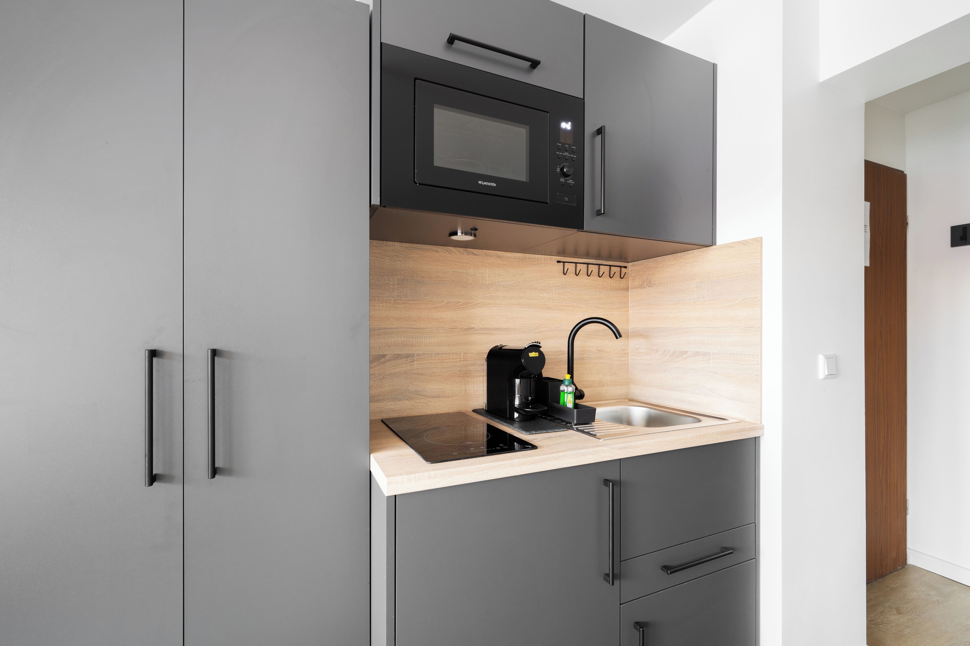 Una cocina compacta con microondas integrado, cafetera y pileta.